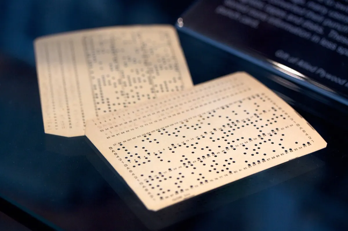 Two cream-colored IBM 96-hole punched cards from 1969 lying in a dark museum display case